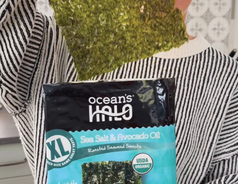 a woman pulling out an extra large seaweed snack from a package labeled as organic XL seaweed snacks. Sea Salt & avocado oil flavor.
